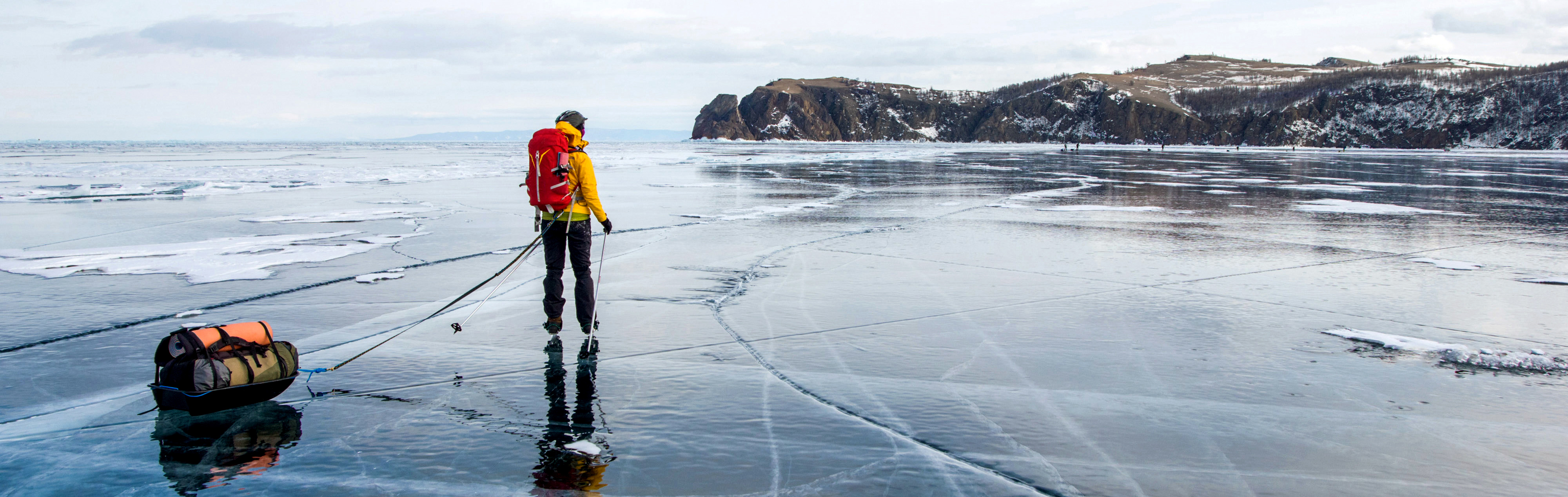 Person på is, fullt utrustad med ryggsäck i skärgårdsmiljö. 
            